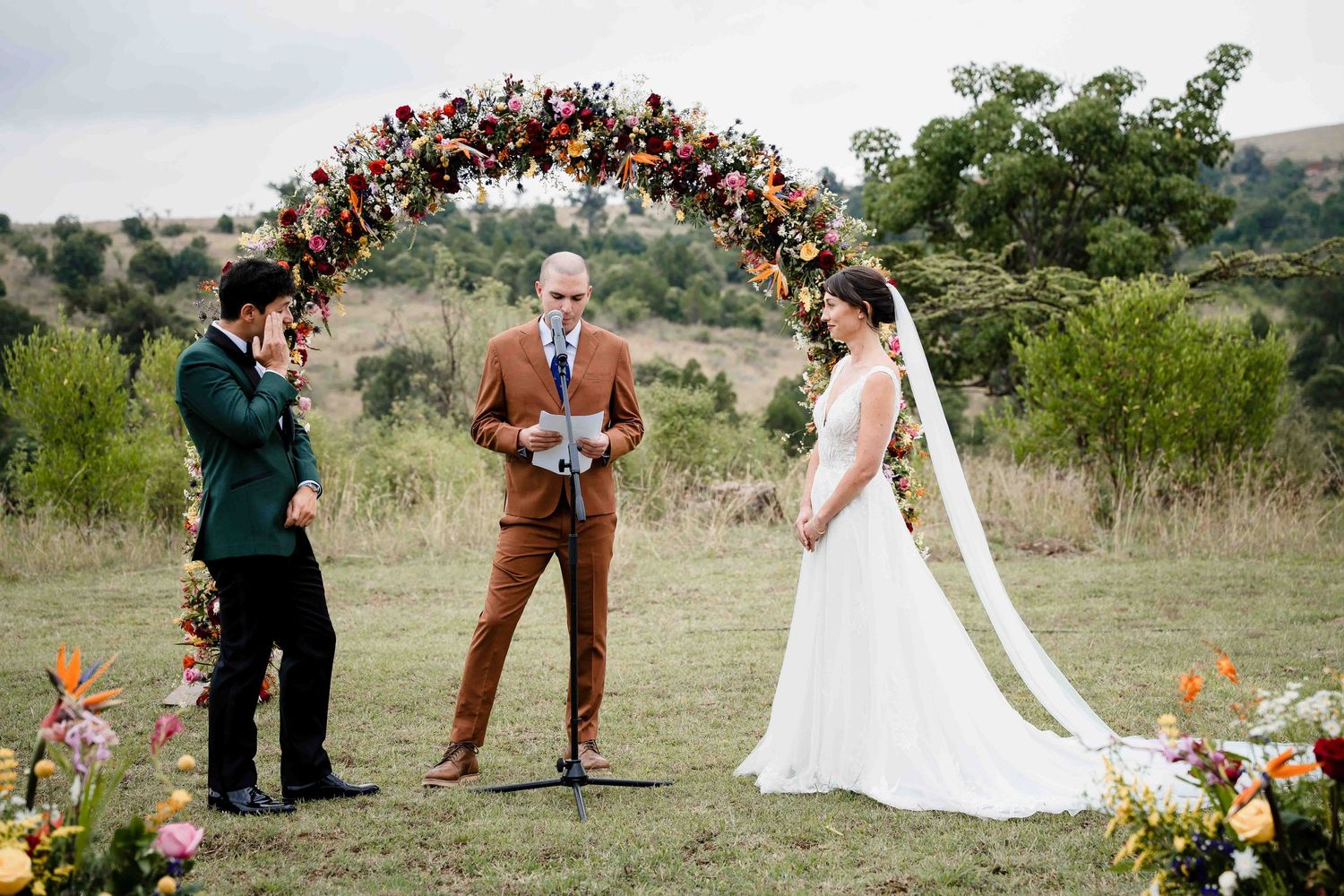 A wedding ceremony setup in a rustic outdoor field with orange and red floral arrangements and natural decor.