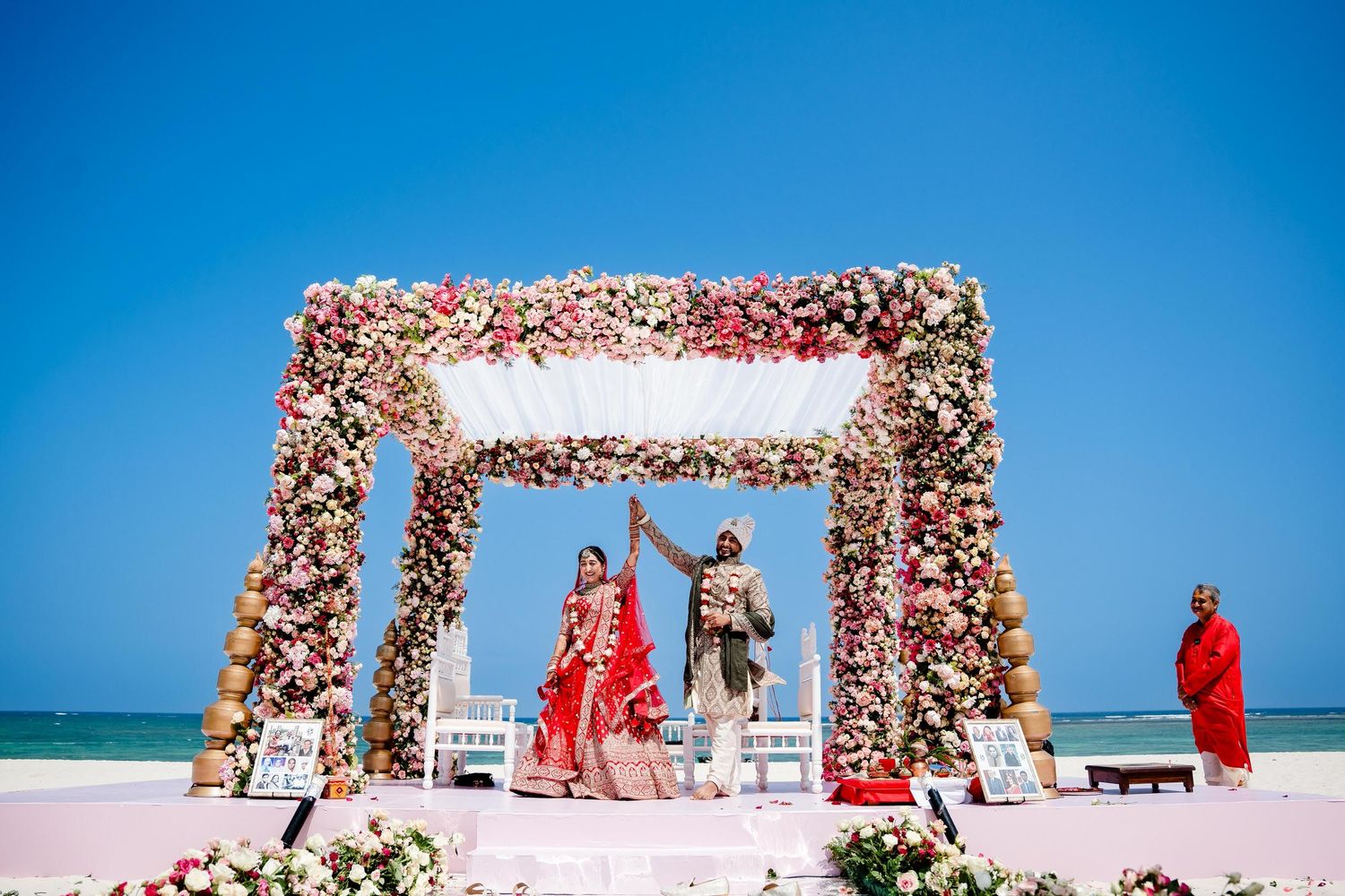 A beachfront wedding ceremony setup with a floral arch and white chairs against a bright blue ocean backdrop.