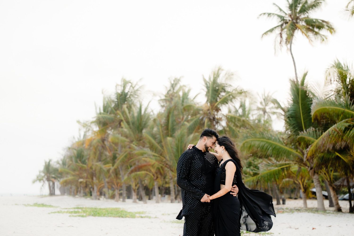 A romantic couple embraces on a palm tree-lined beach during a tropical photoshoot session.
