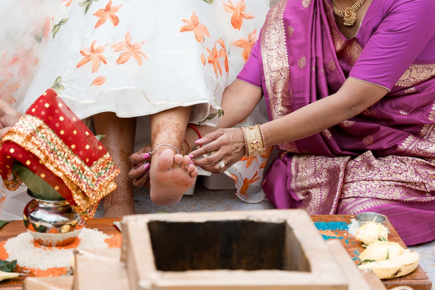 Hands adorned with traditional Indian jewelry and henna perform cultural rituals during a wedding ceremony.