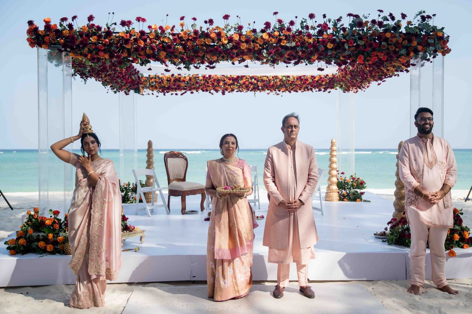 Wedding party in peach-colored attire poses playfully in sequence against a beachfront backdrop with red floral decor.