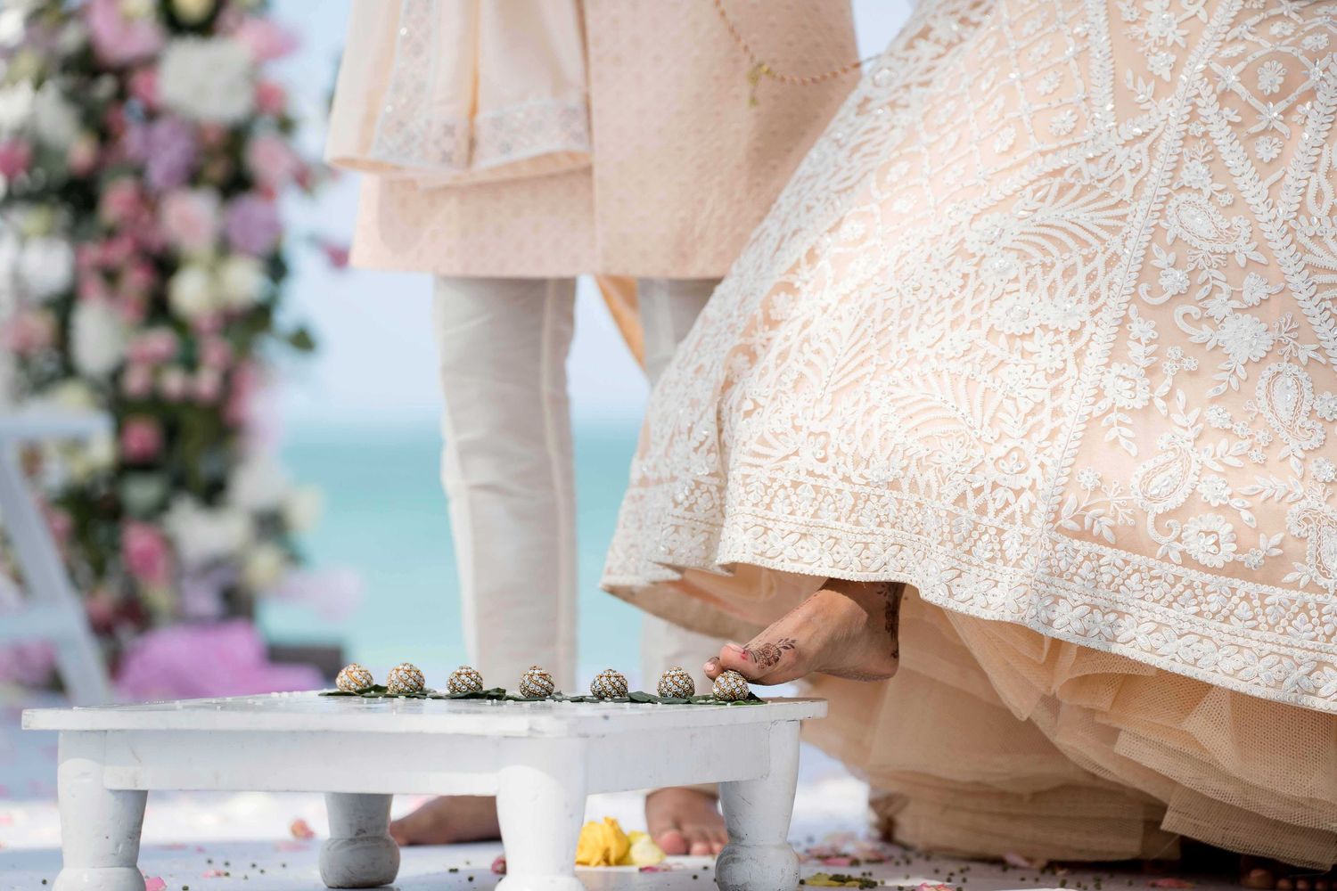 Elegant wedding cake with intricate lace details and floral decorations displayed at an indoor reception venue.