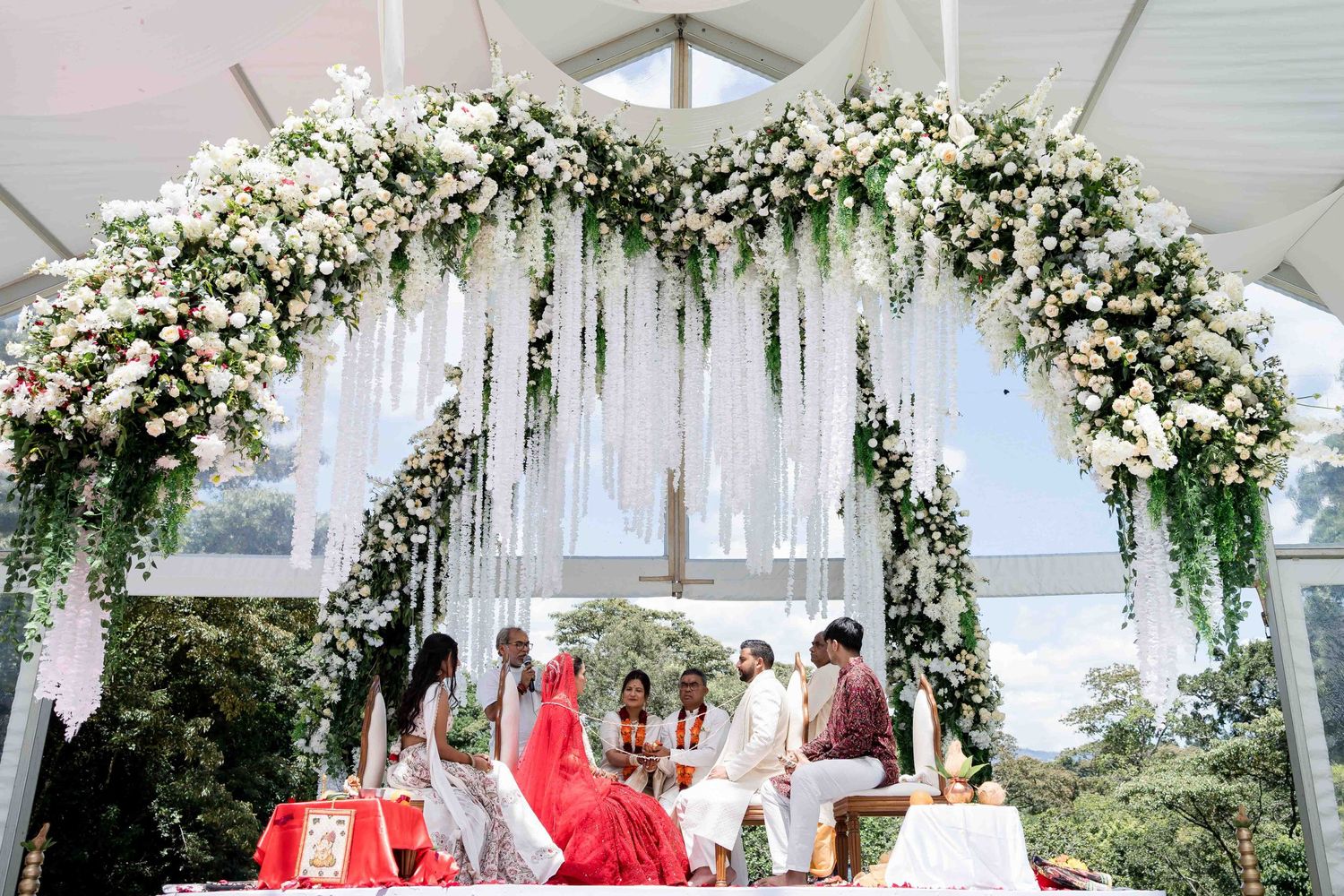 Elegant white floral arch with cascading decorations at an outdoor wedding ceremony setup.
