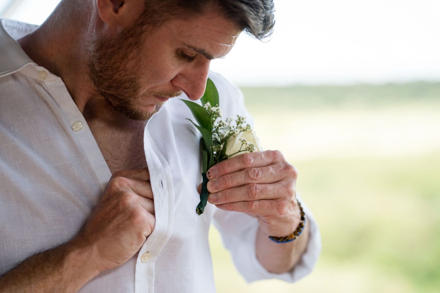 A white boutonniere is carefully pinned to formal attire outdoors.