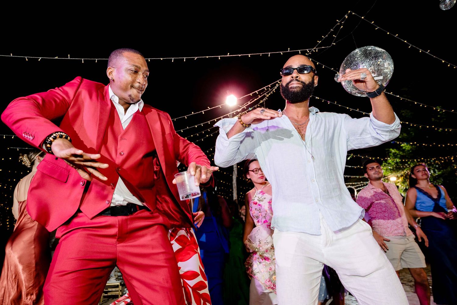 People dancing and celebrating at a lively party with string lights overhead.