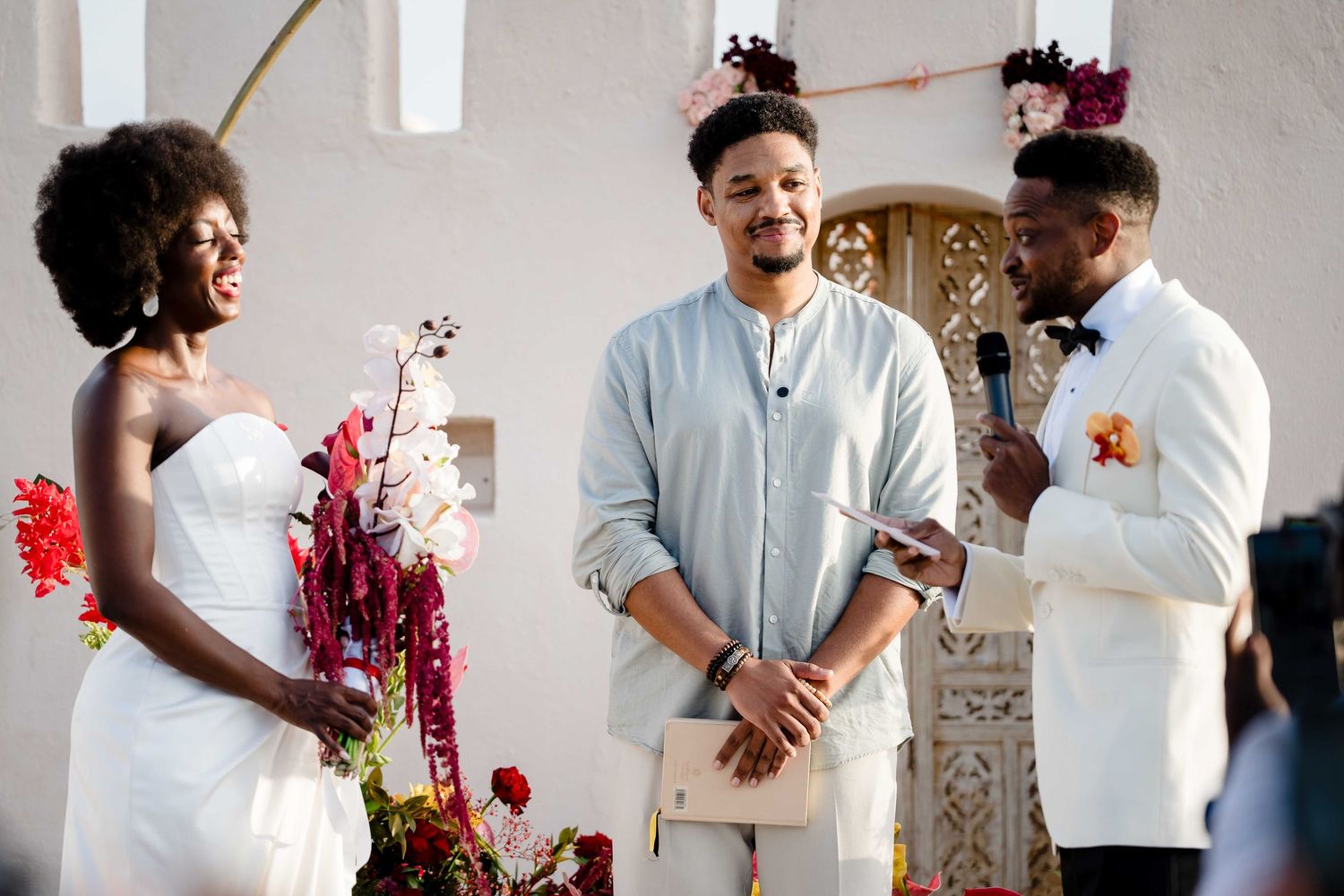 Couple in white outfits decorating with red flowers and foliage in a bright modern interior space.
