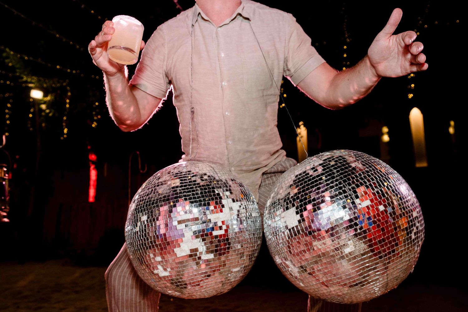 Disco balls being held up in a dark nightclub setting with colorful lights in the background.