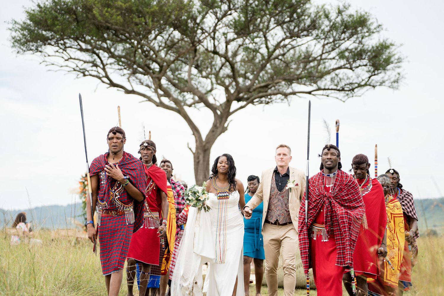 Wedding party poses with Maasai warriors in traditional dress on the African savanna.