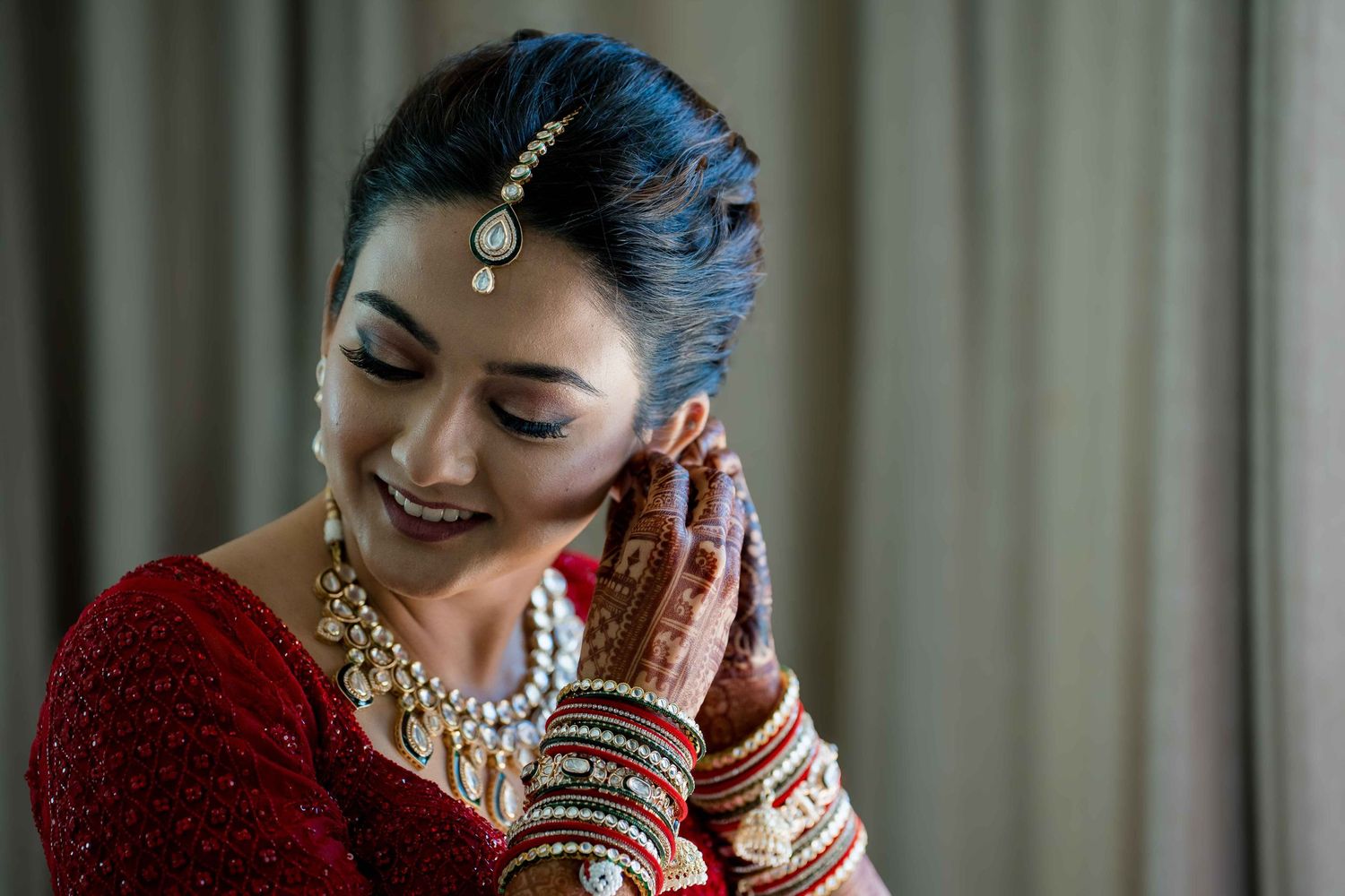 Traditional bridal portrait showcasing intricate jewelry and henna-adorned hands in red attire.