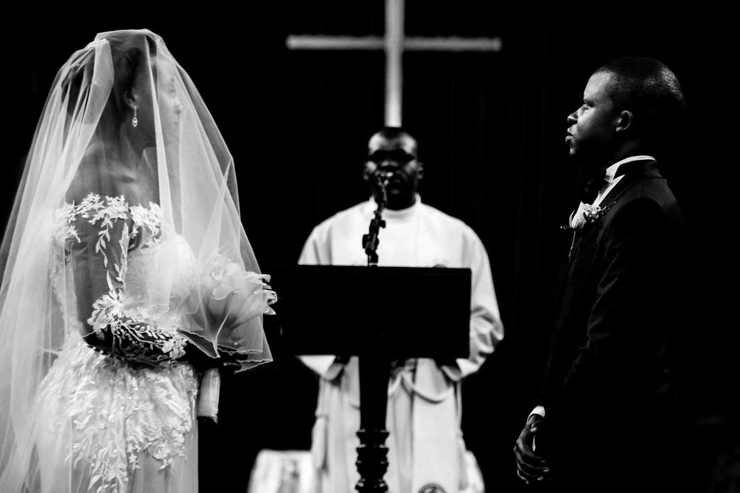Black and white church wedding ceremony with cross visible in background.
