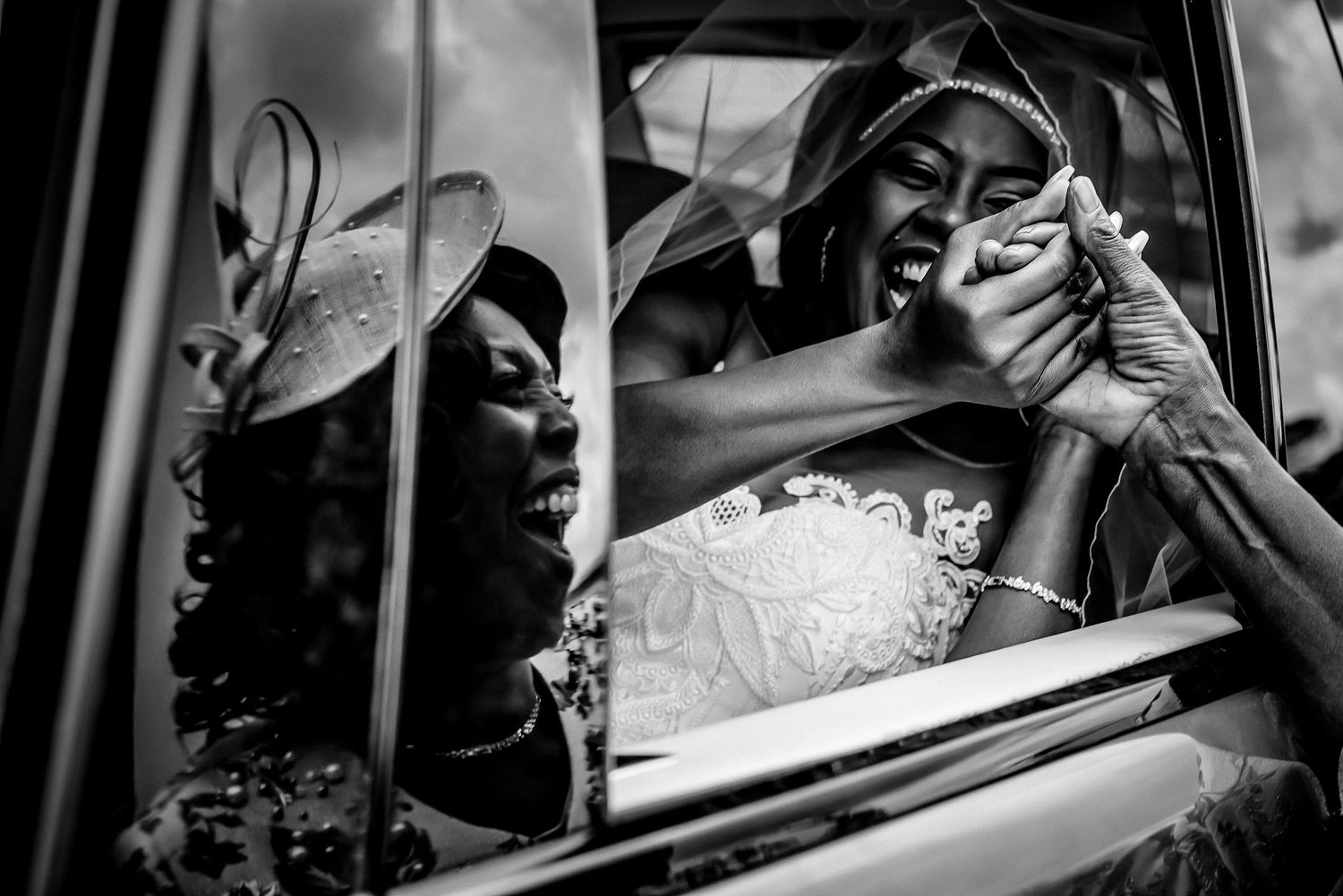 Wedding party members share candid moments through a car window in black and white photography.