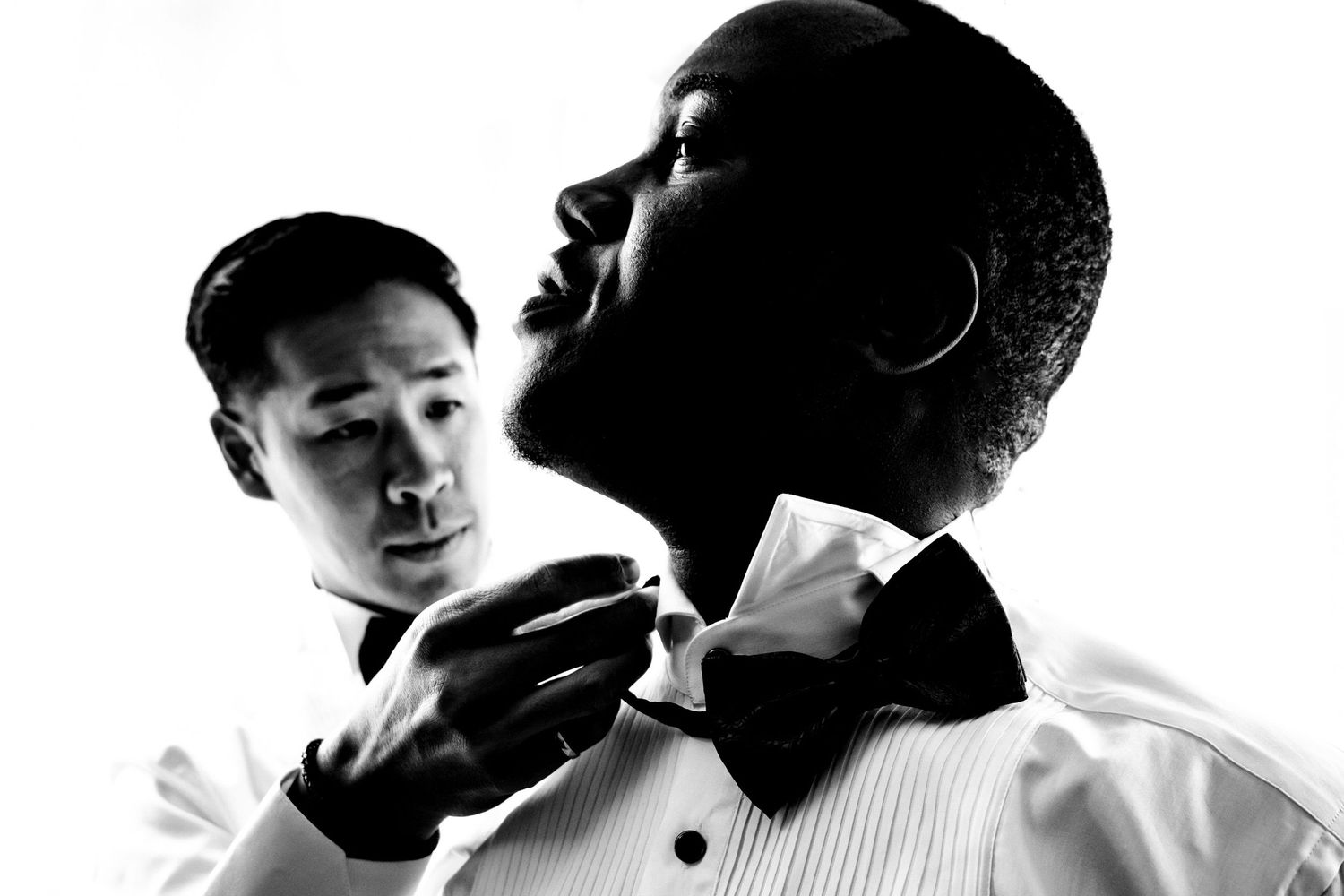 Black and white portrait of two men in formal attire adjusting a bowtie.