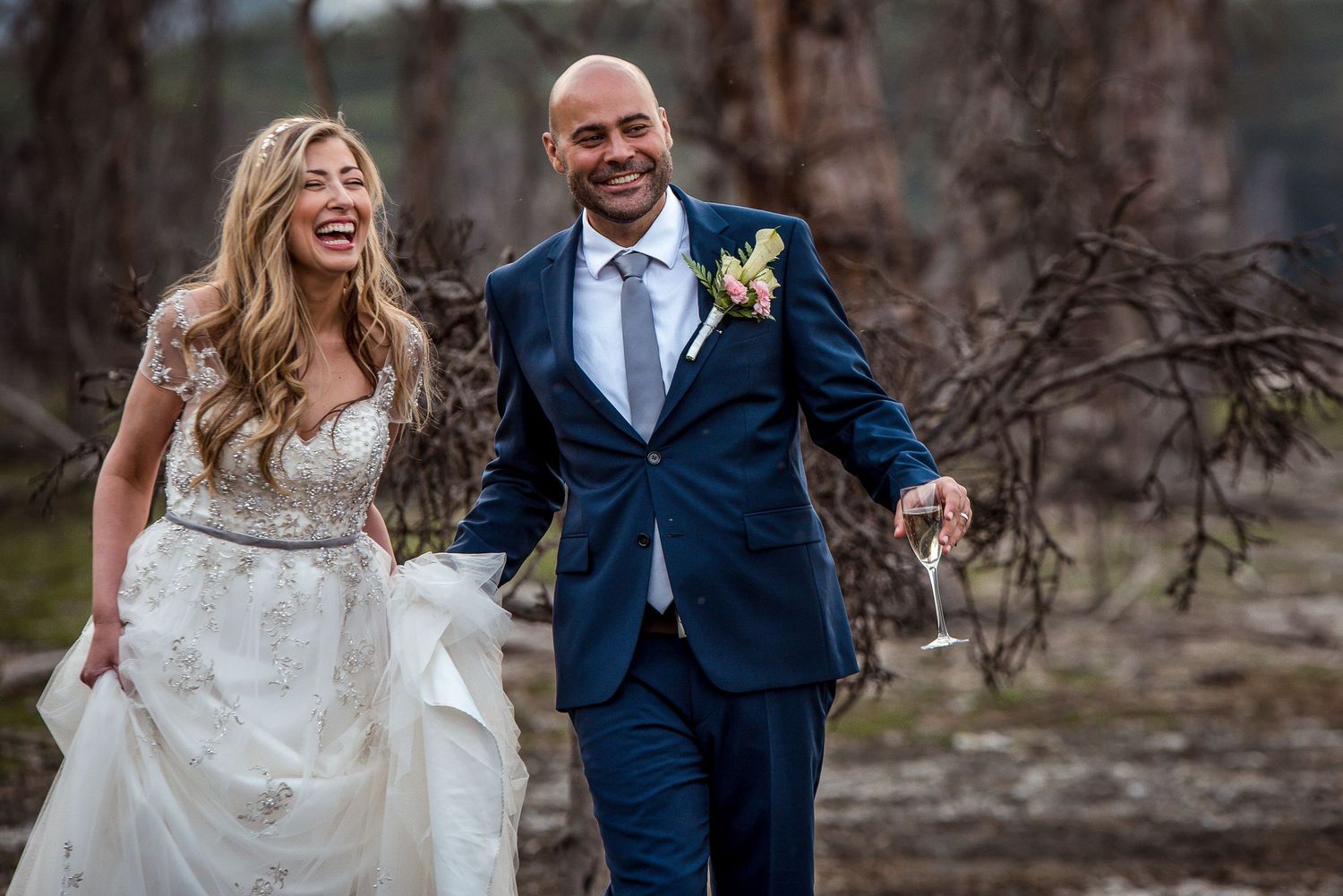 Couple walking and laughing together in formal attire through autumn scenery.