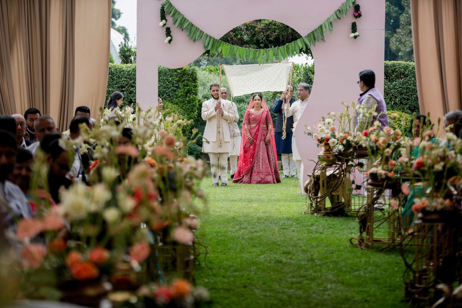 Outdoor wedding ceremony with floral decorations lining the aisle and draped fabric canopy.