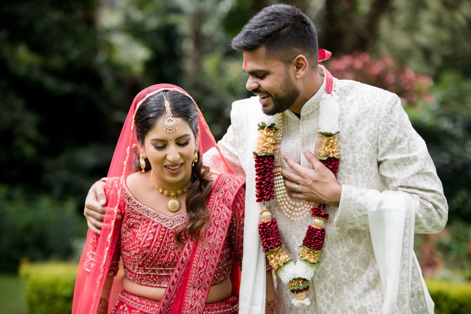 Couple in traditional Indian wedding attire sharing a joyful moment in a garden.