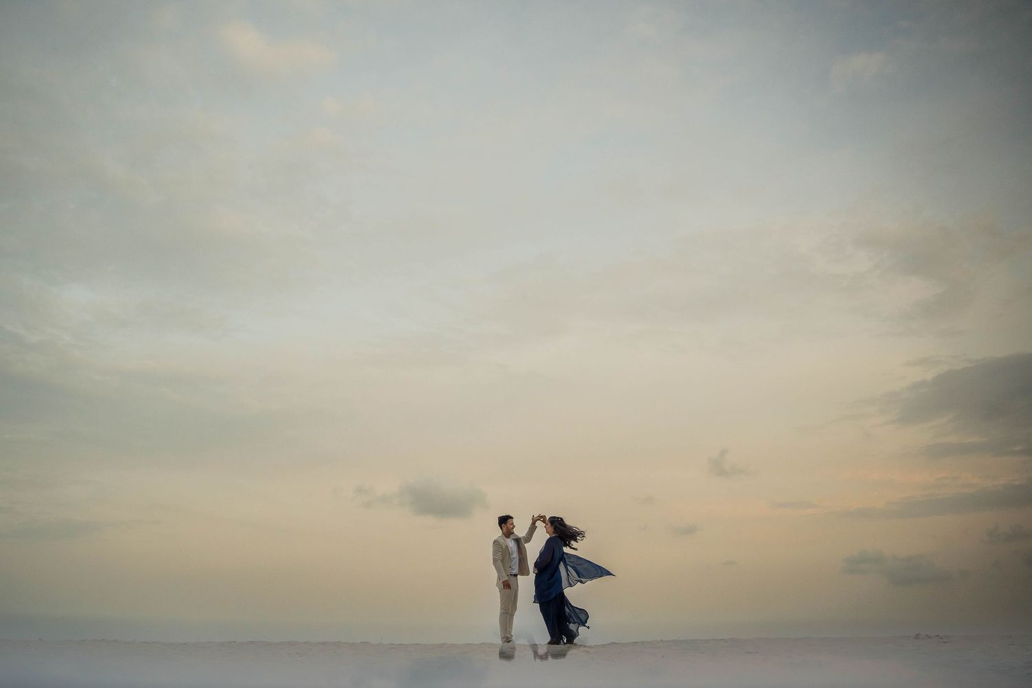A silhouetted couple walks along a beach at sunset with dramatic cloudy skies in the background.