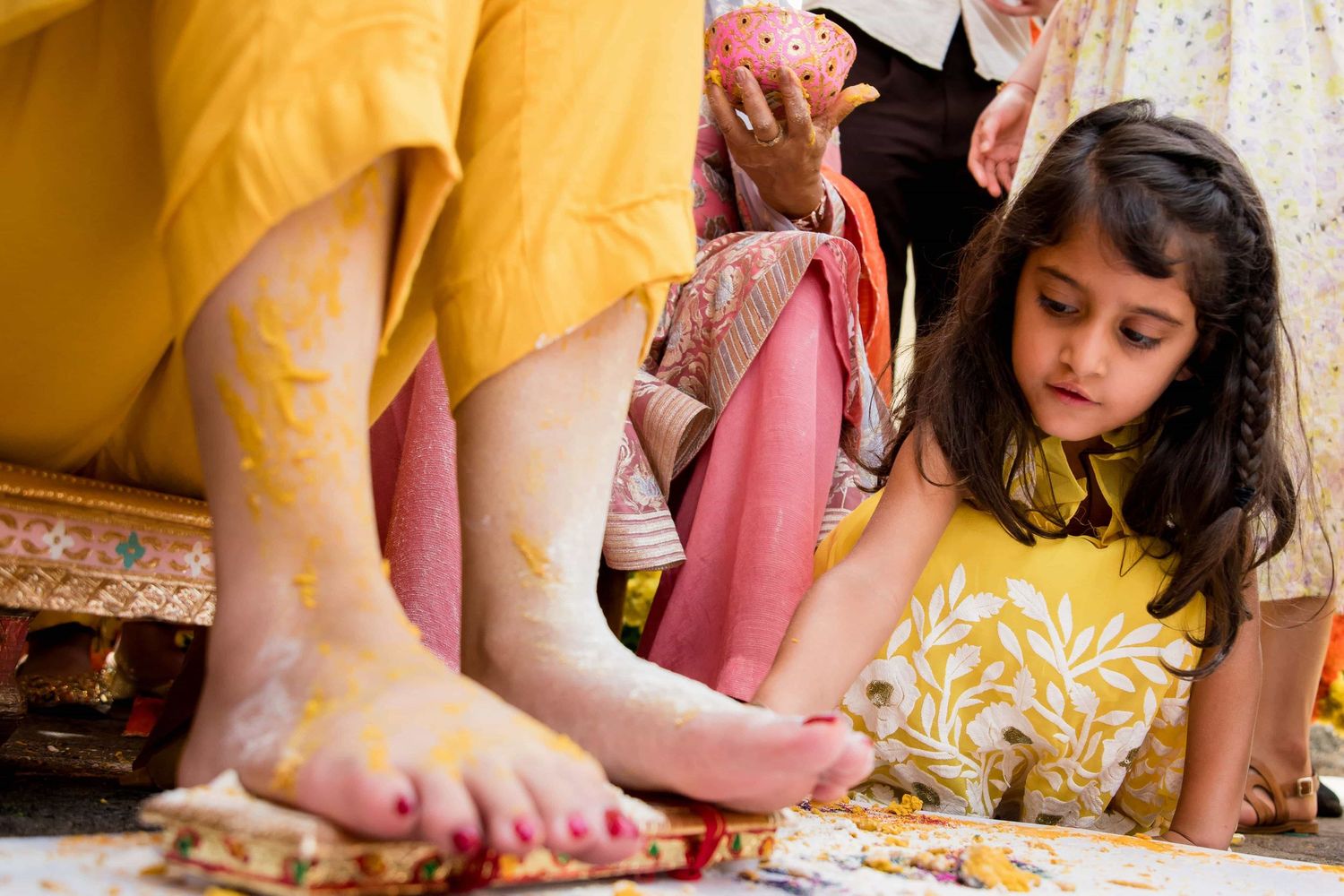 Young child in yellow dress creating art with colorful paints on the floor.