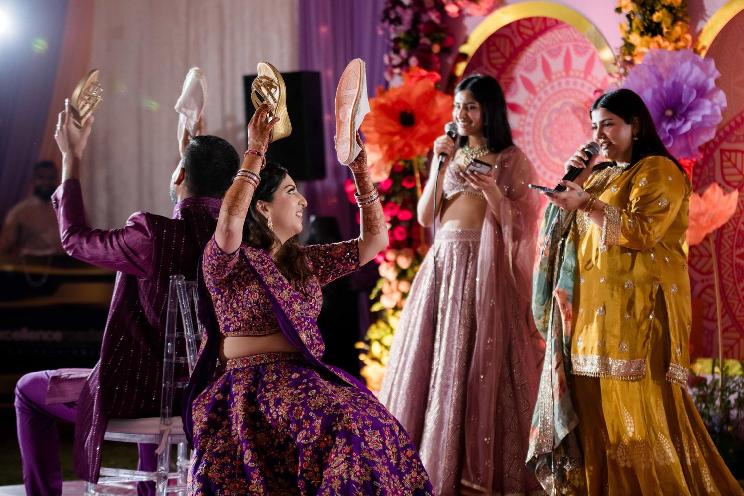 Guests in colorful traditional outfits dance during an Indian celebration with vibrant decorations.