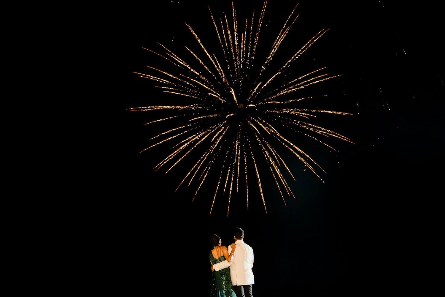 A couple watches a large golden firework burst in the night sky during a romantic moment.