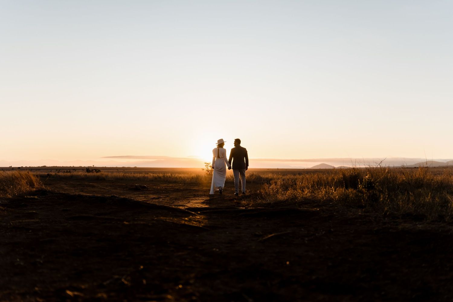 Two silhouettes stand together against a golden sunset over rolling hills.