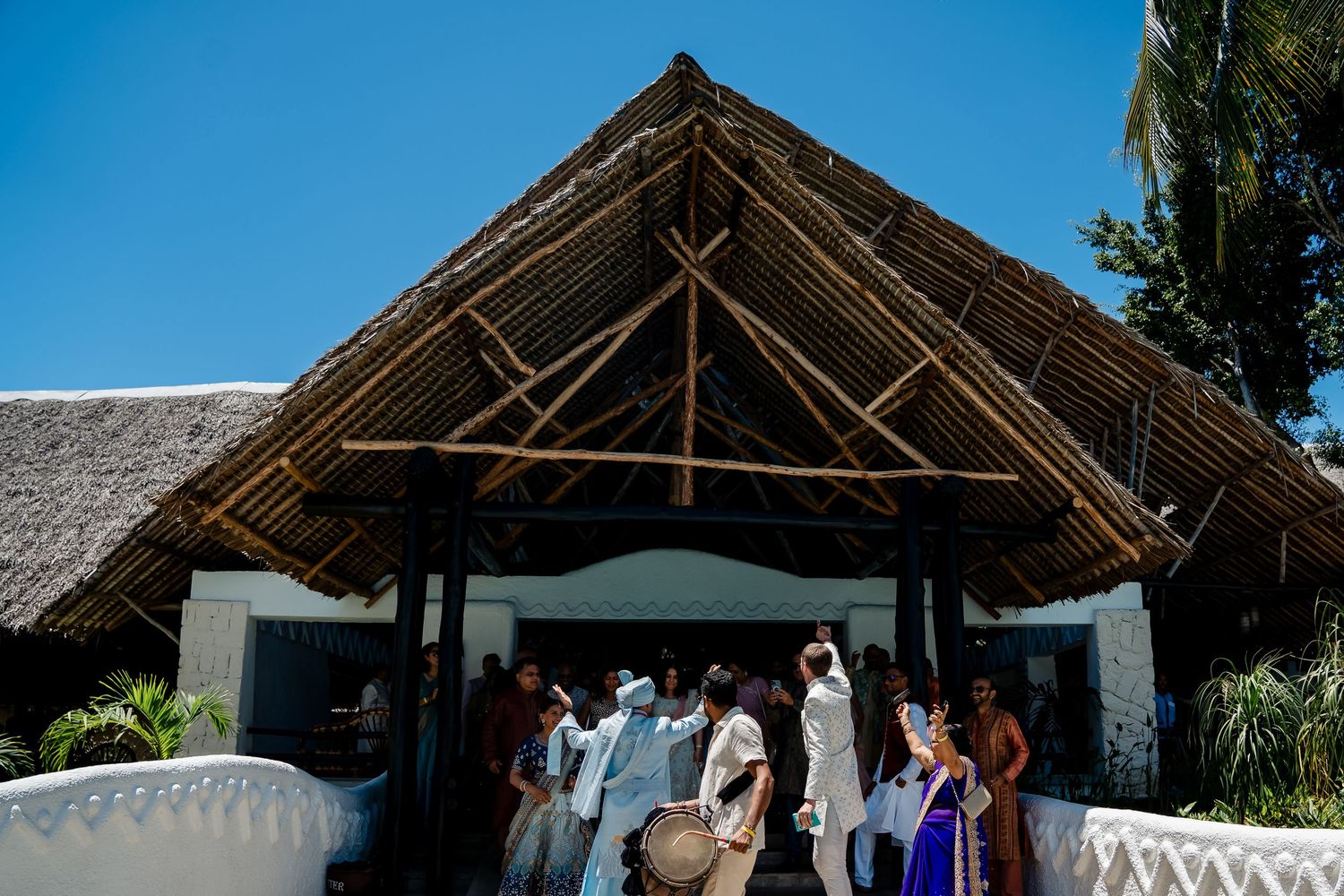 A group gathers under a thatched-roof entrance at a tropical venue during a celebration.