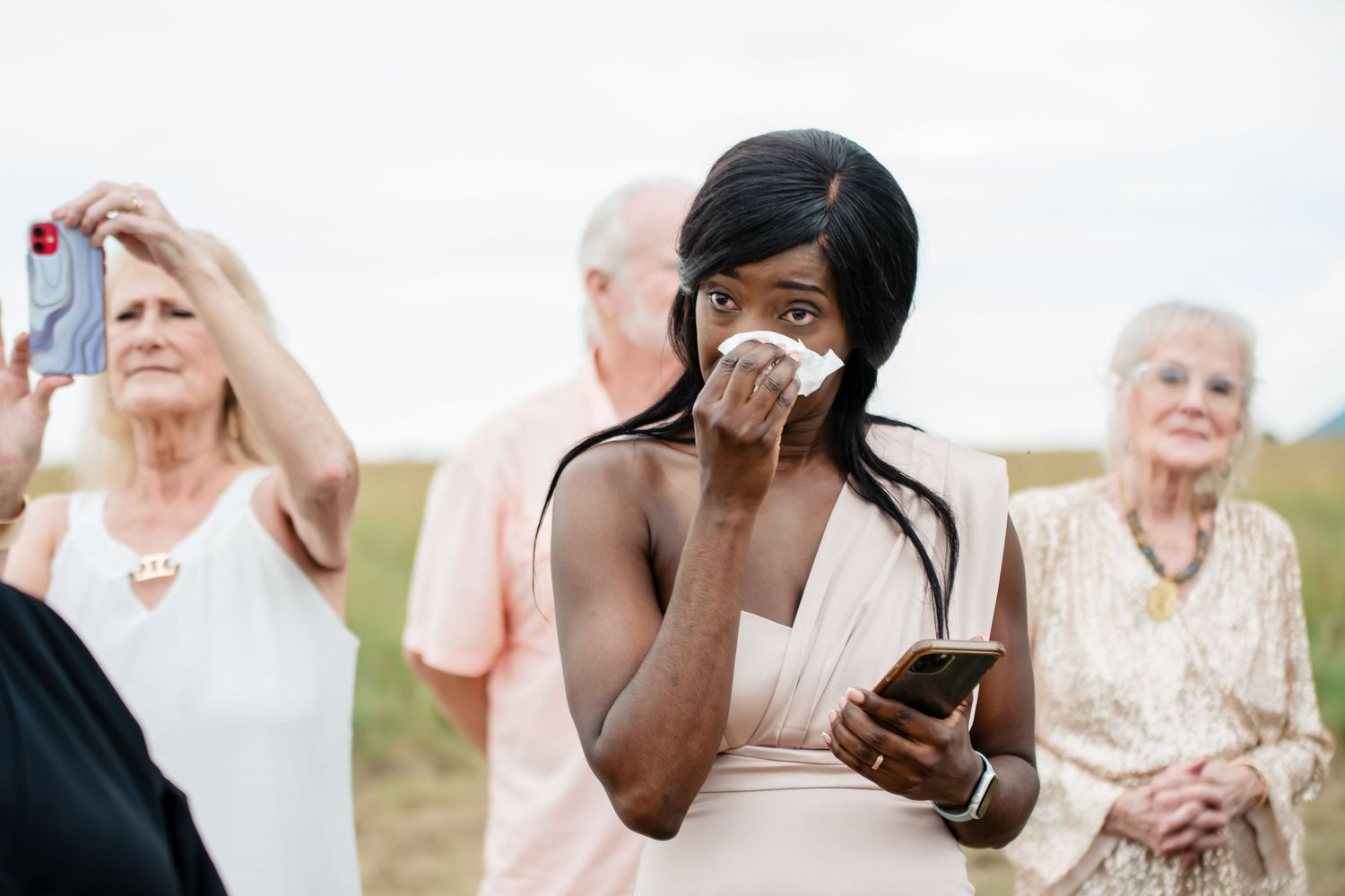 Emotional reactions as guests use phones to capture moments at an outdoor event.