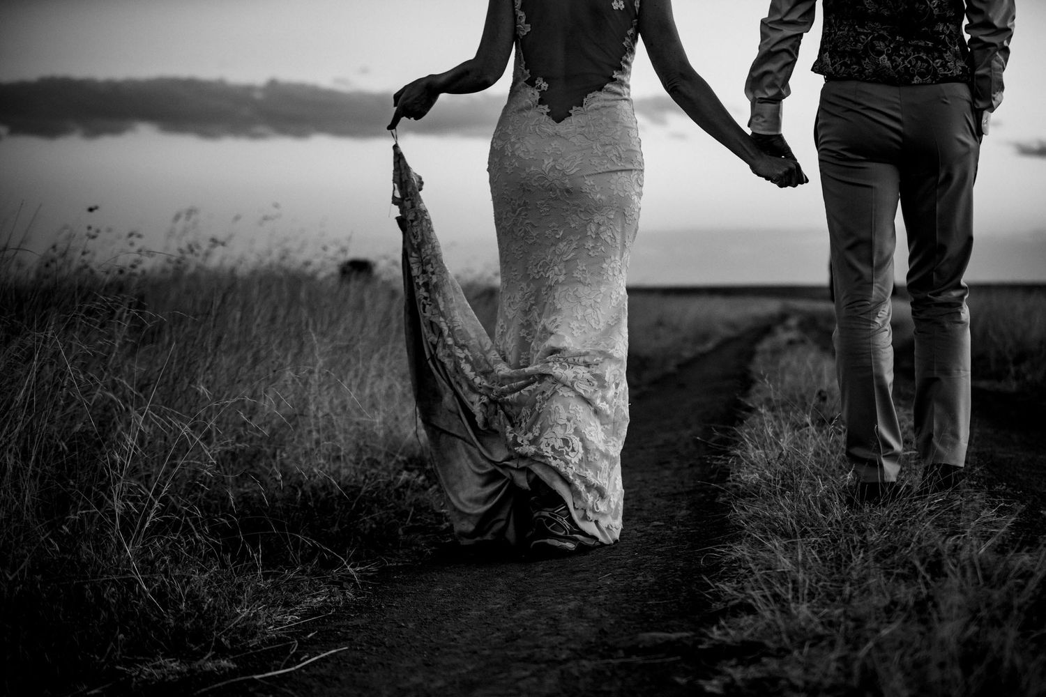 Artistic black and white photo of people walking through tall grass at dusk.