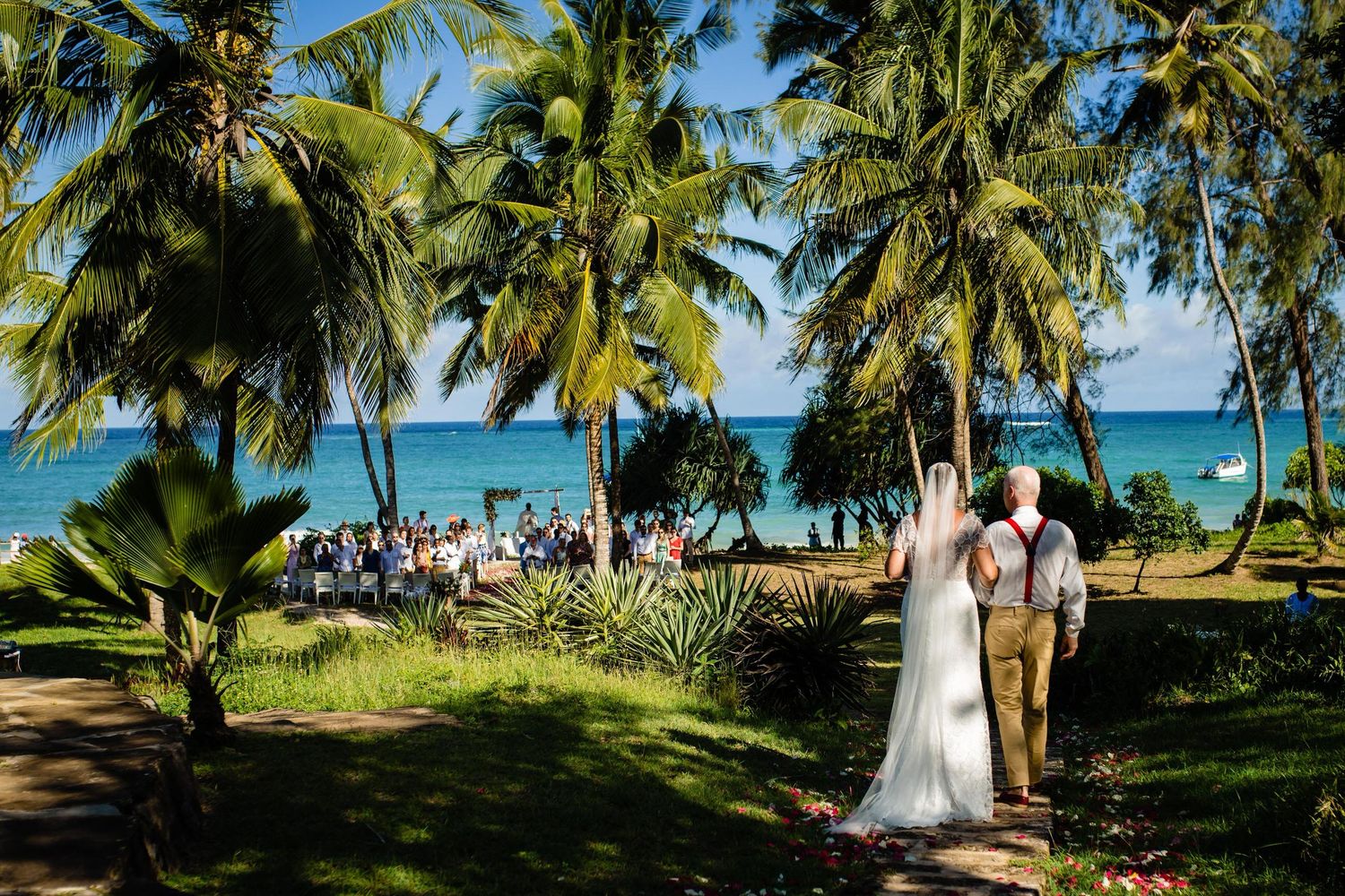 Tropical beach wedding ceremony setup with palm trees and ocean view in the background.