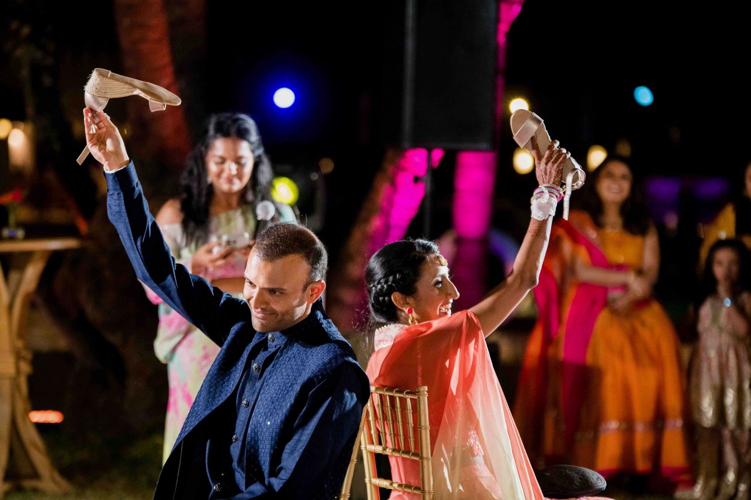 Newly married couple dances during their first dance at a wedding reception with colorful lights in background.