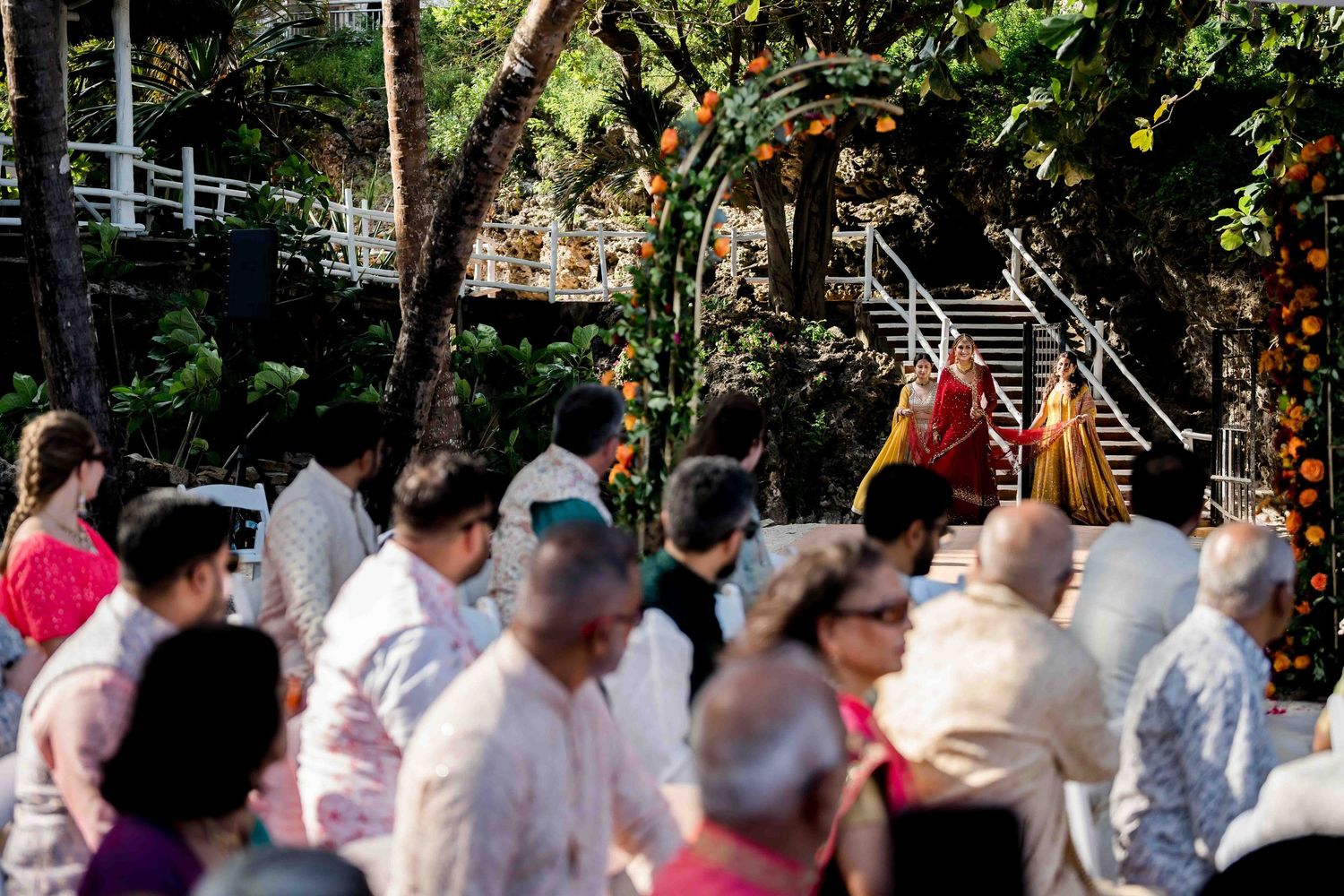 A large crowd of wedding guests gathered outdoors under trees at a festive celebration.