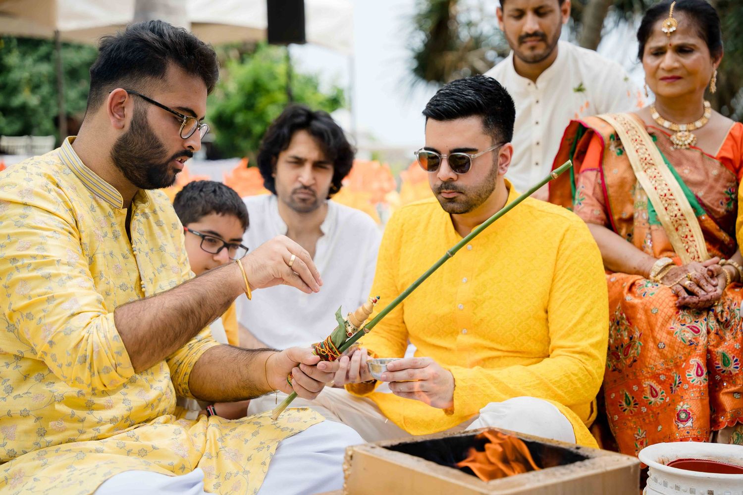 A group celebrates during an Indian wedding ceremony wearing traditional yellow and orange attire.