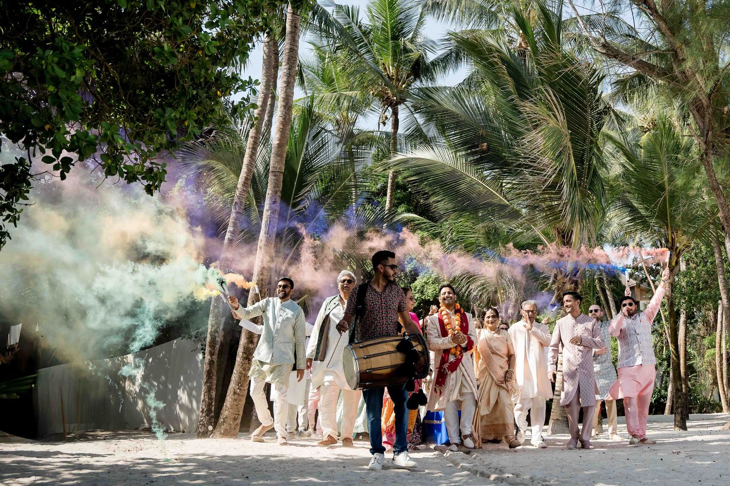 A colorful smoke bomb celebration creates a vibrant atmosphere along a palm tree-lined path with people gathered outdoors.