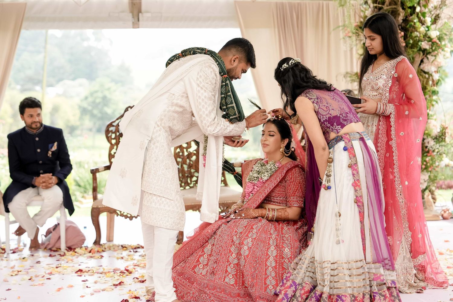 Traditional Indian wedding ceremony with people gathered around during a ritual on rose petal covered floor.