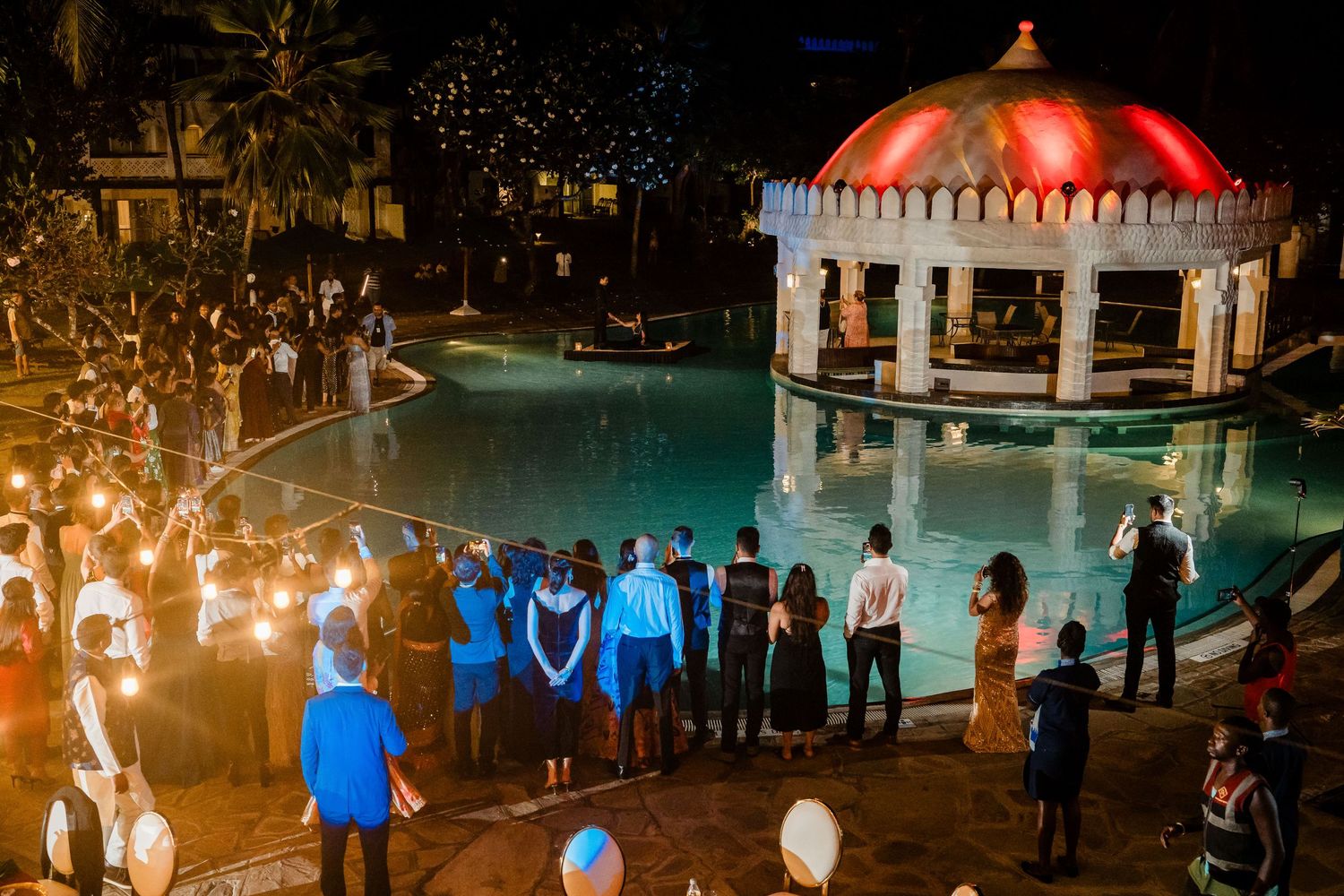 Evening gathering around an illuminated poolside gazebo with guests holding sparklers.
