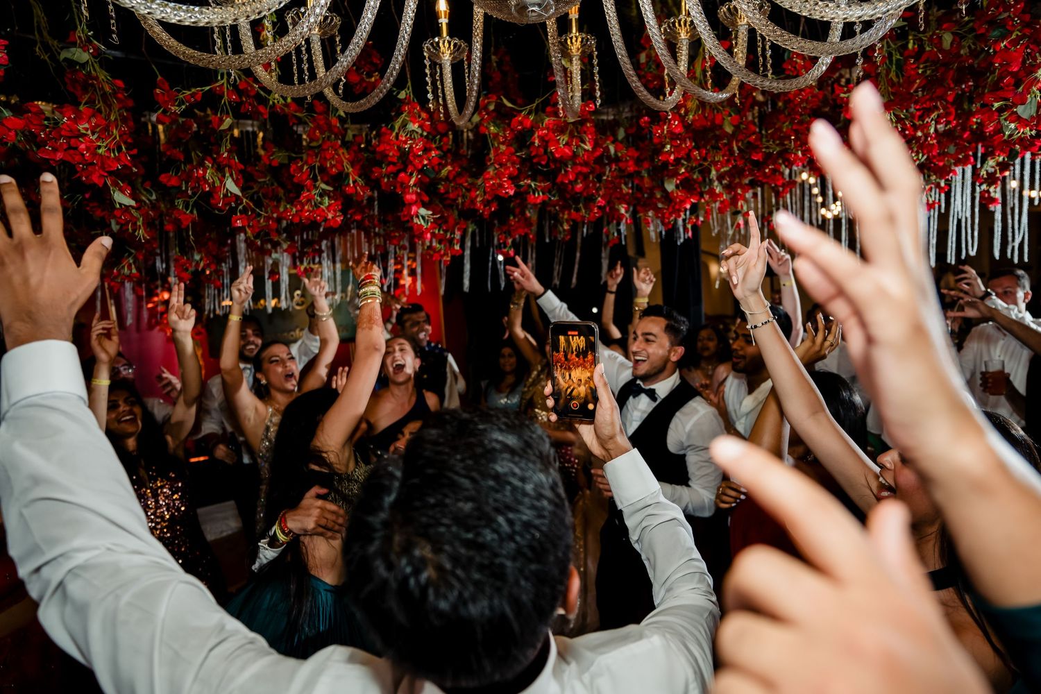 Crowd raises hands in celebration under dramatic red floral ceiling decor.