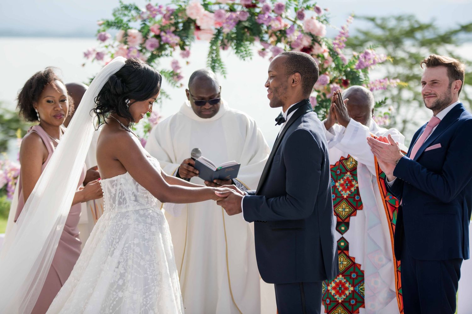 A wedding ceremony taking place under a floral arch with pink blooms.
