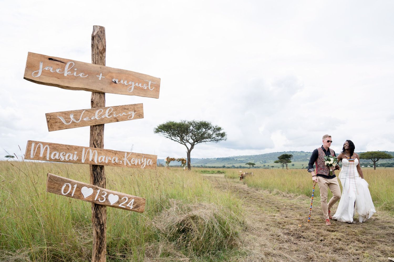 Rustic wooden directional wedding sign with couple in background on African plains.