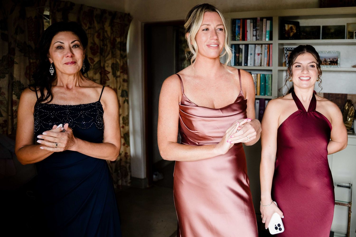 A group of people in formal attire gather at an indoor event wearing pink, burgundy and navy dresses.
