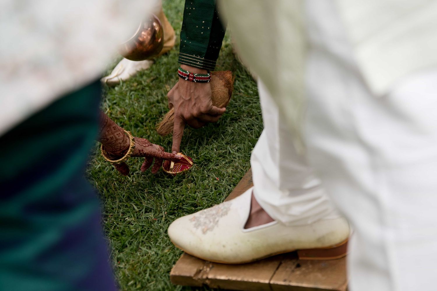Close-up detail of traditional footwear and anklets on grass during a wedding ceremony.