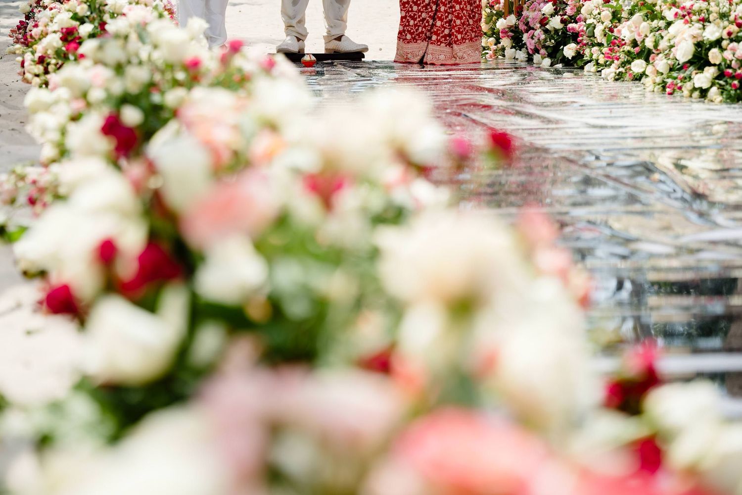 Pink and red flowers create a romantic border along a stone pathway in a garden setting.