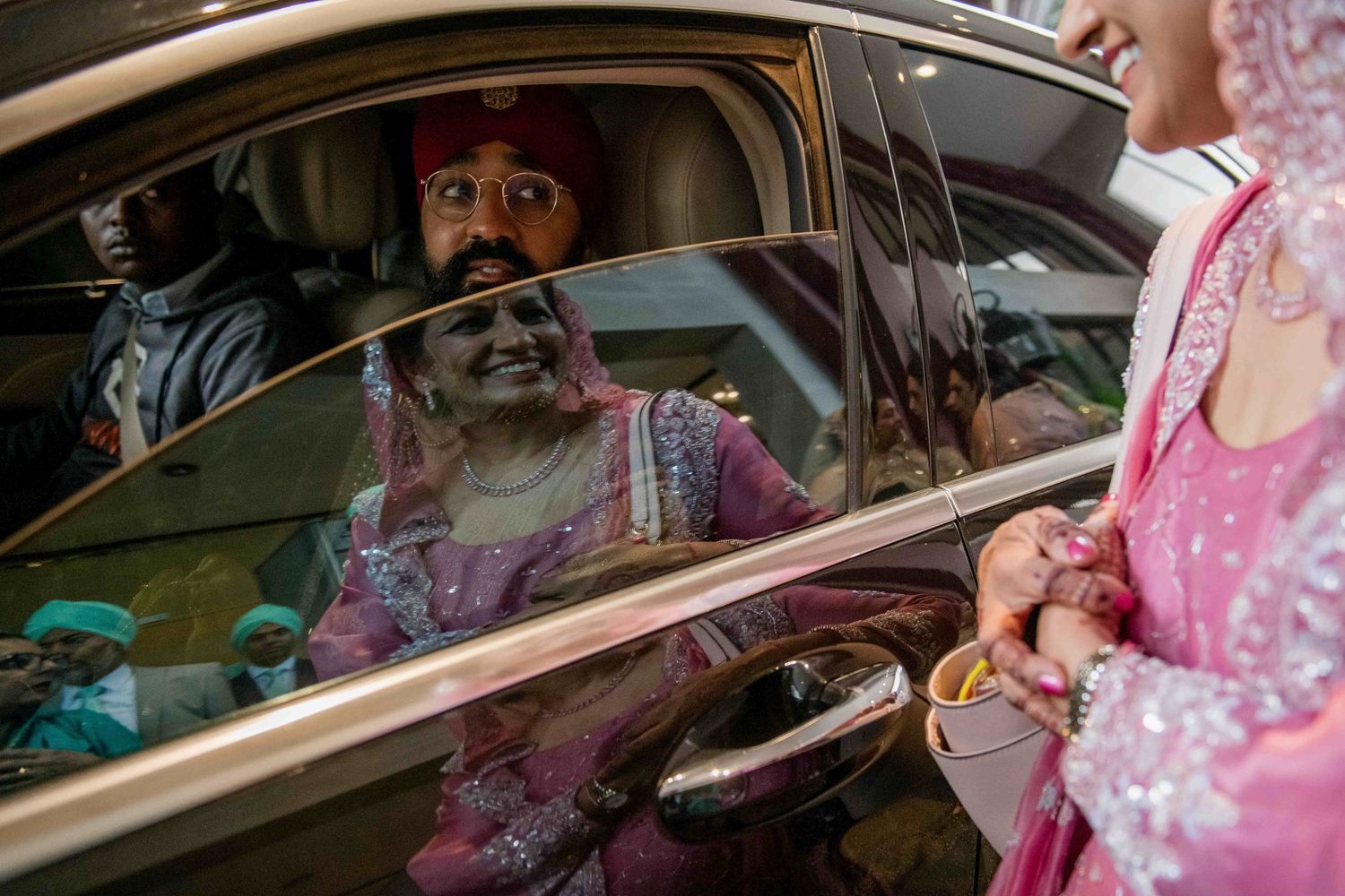 Candid shot through car window during Indian wedding celebrations with guests in colorful attire.