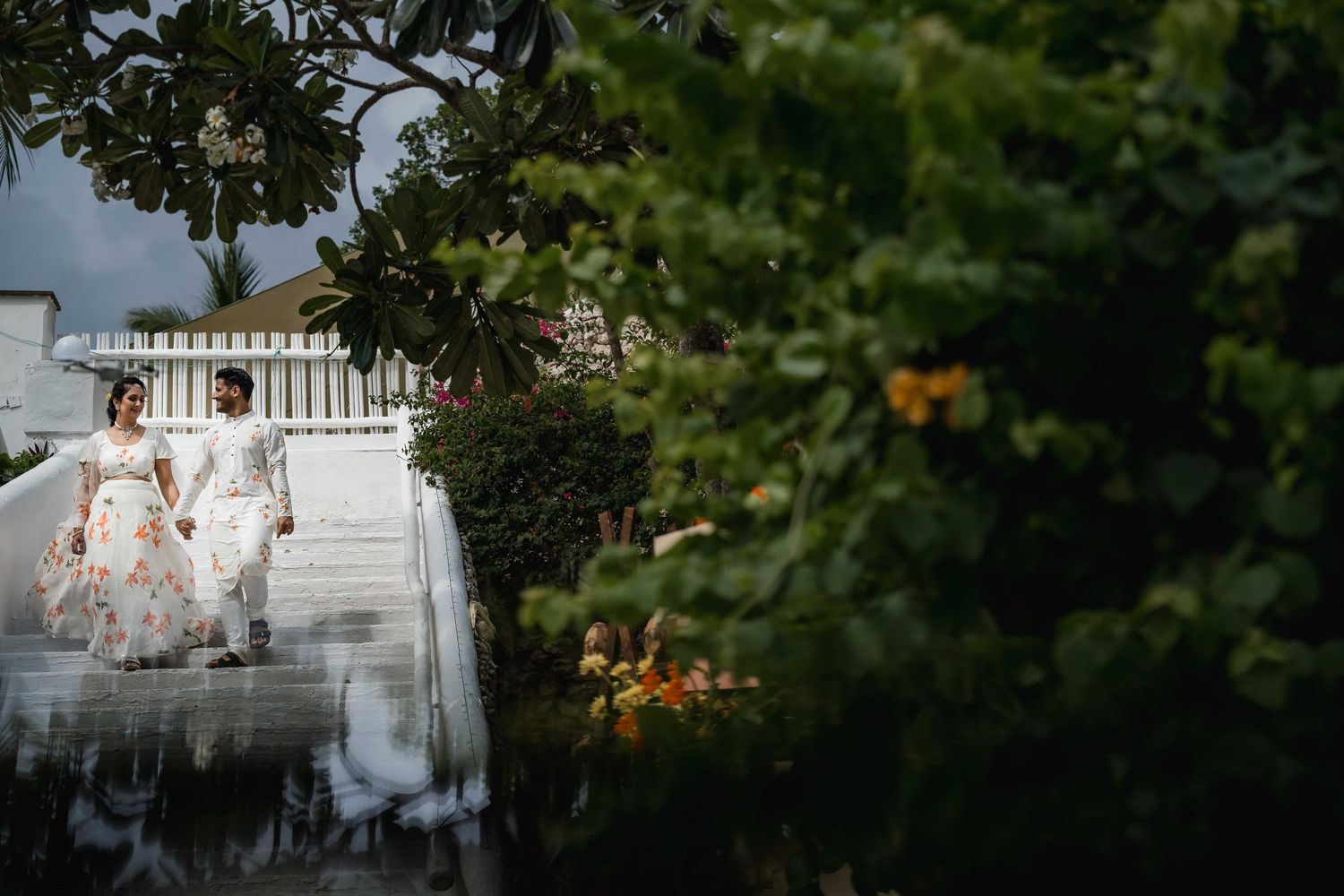 Wedding party in white dresses poses on grand outdoor staircase surrounded by lush greenery.