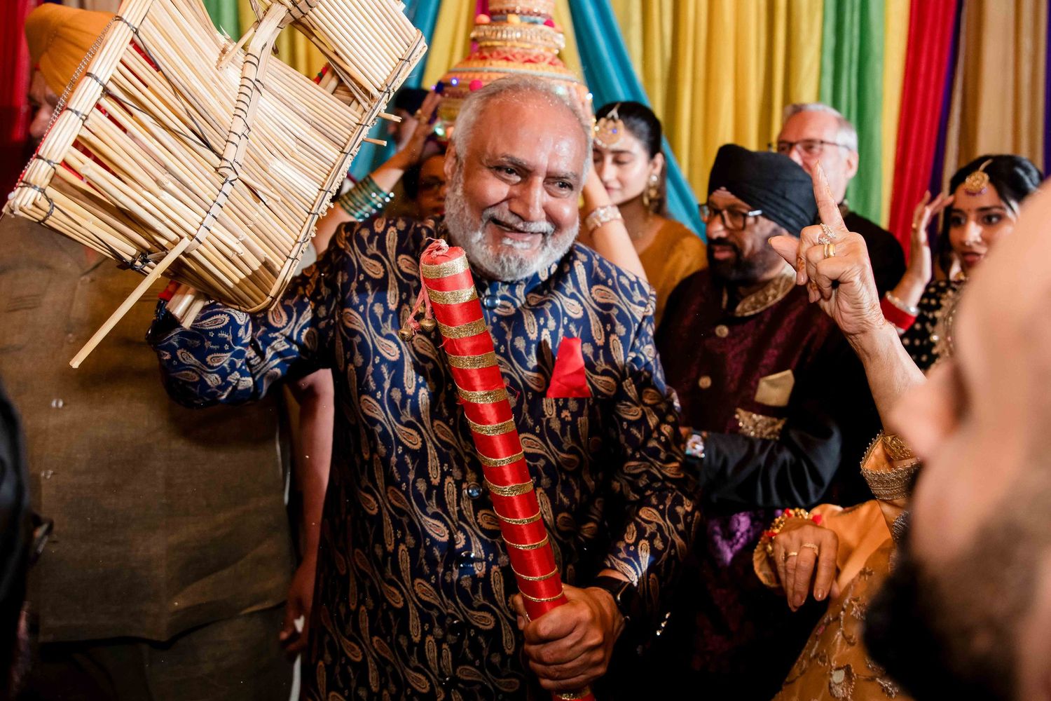Elder guest dancing with musical instrument during festive Indian celebration.