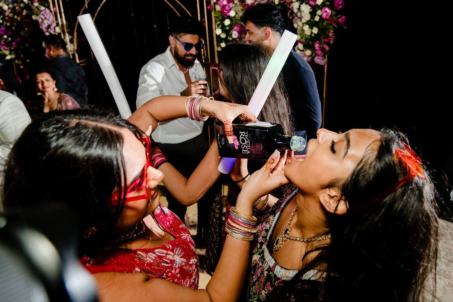 People dance and celebrate at a lively wedding reception party with colorful lighting and decorations.