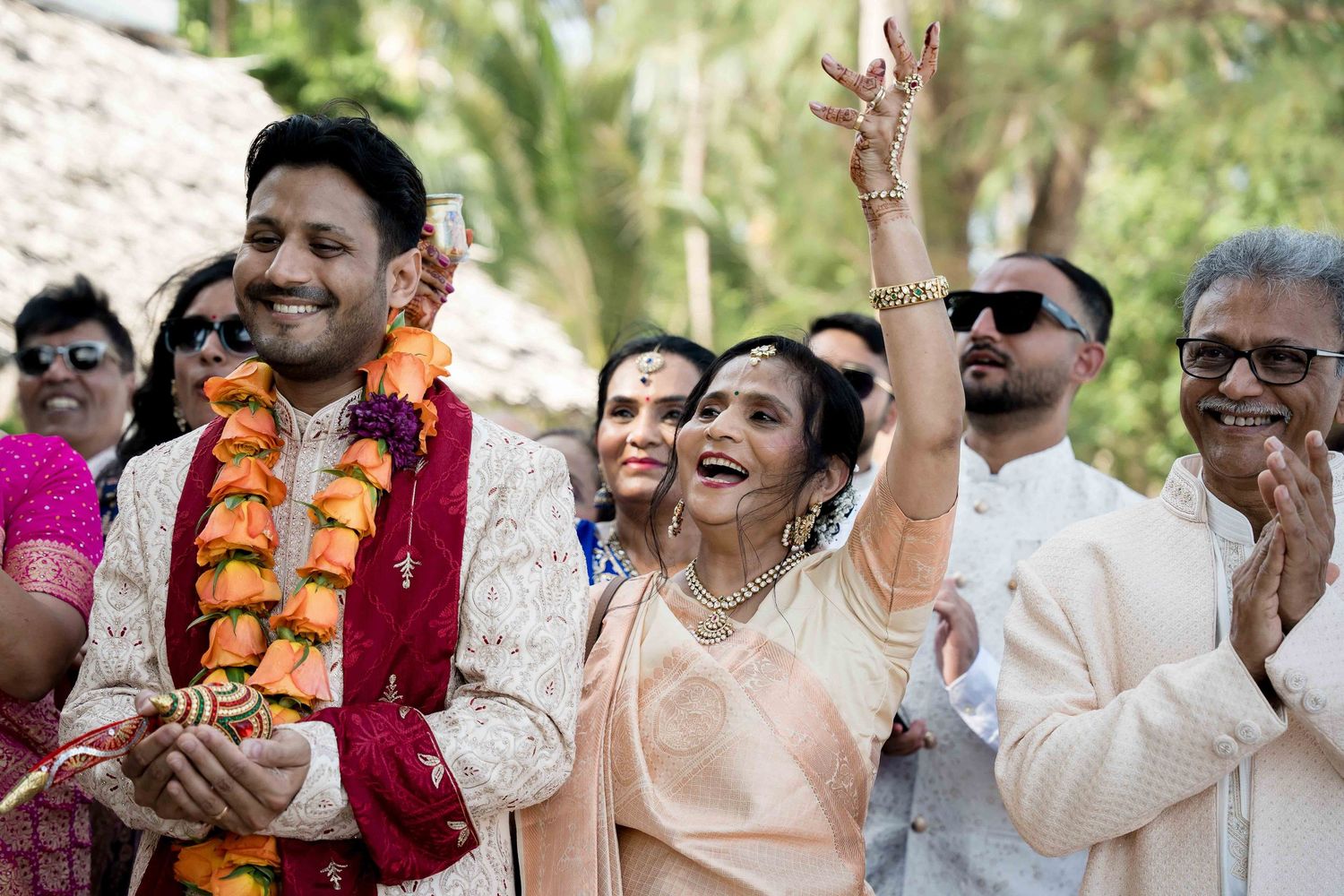 Joyful celebration at an outdoor Indian wedding ceremony with guests wearing traditional attire and floral garlands.