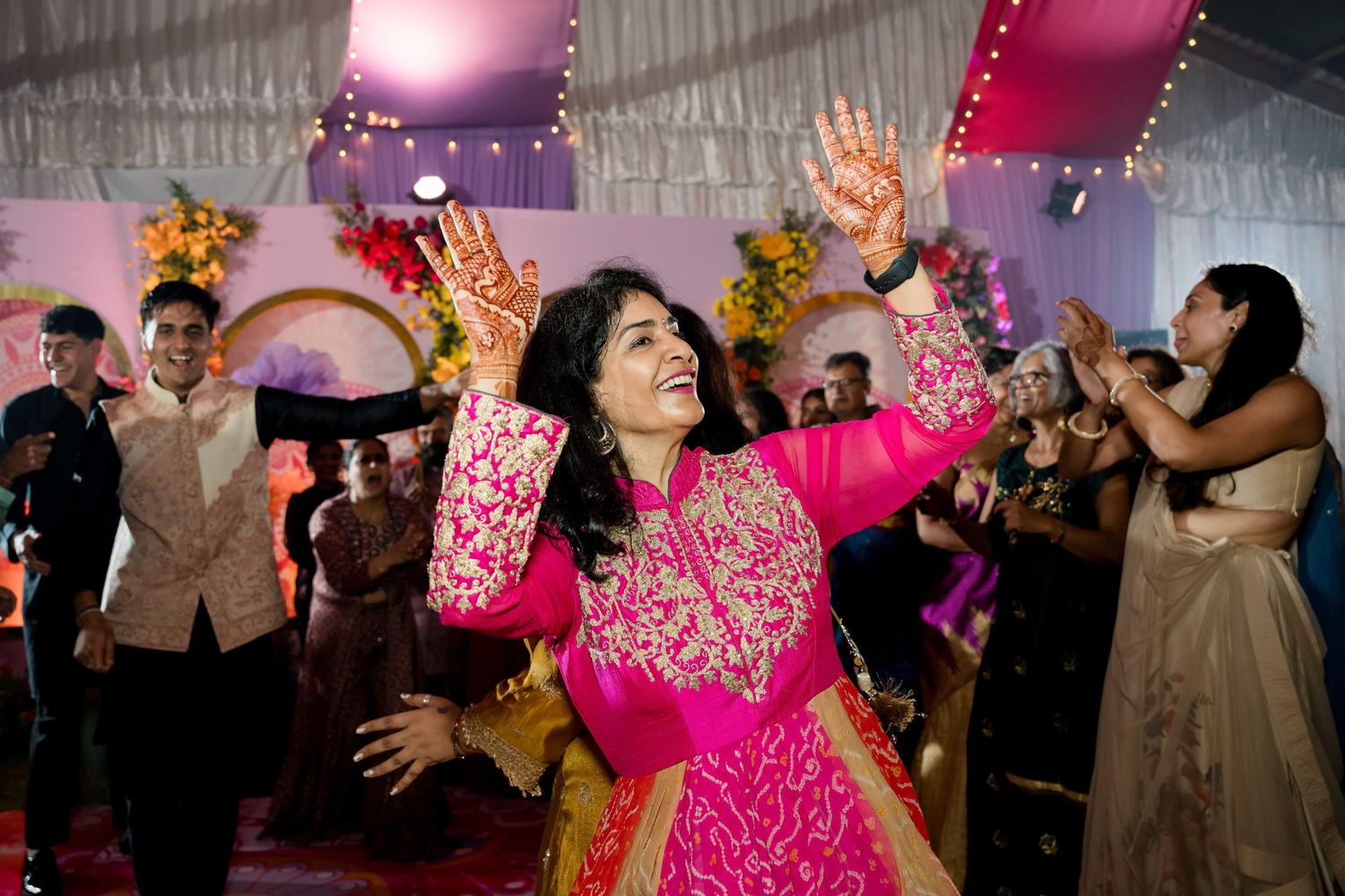 A guest in bright pink attire dances joyfully at an Indian wedding celebration.