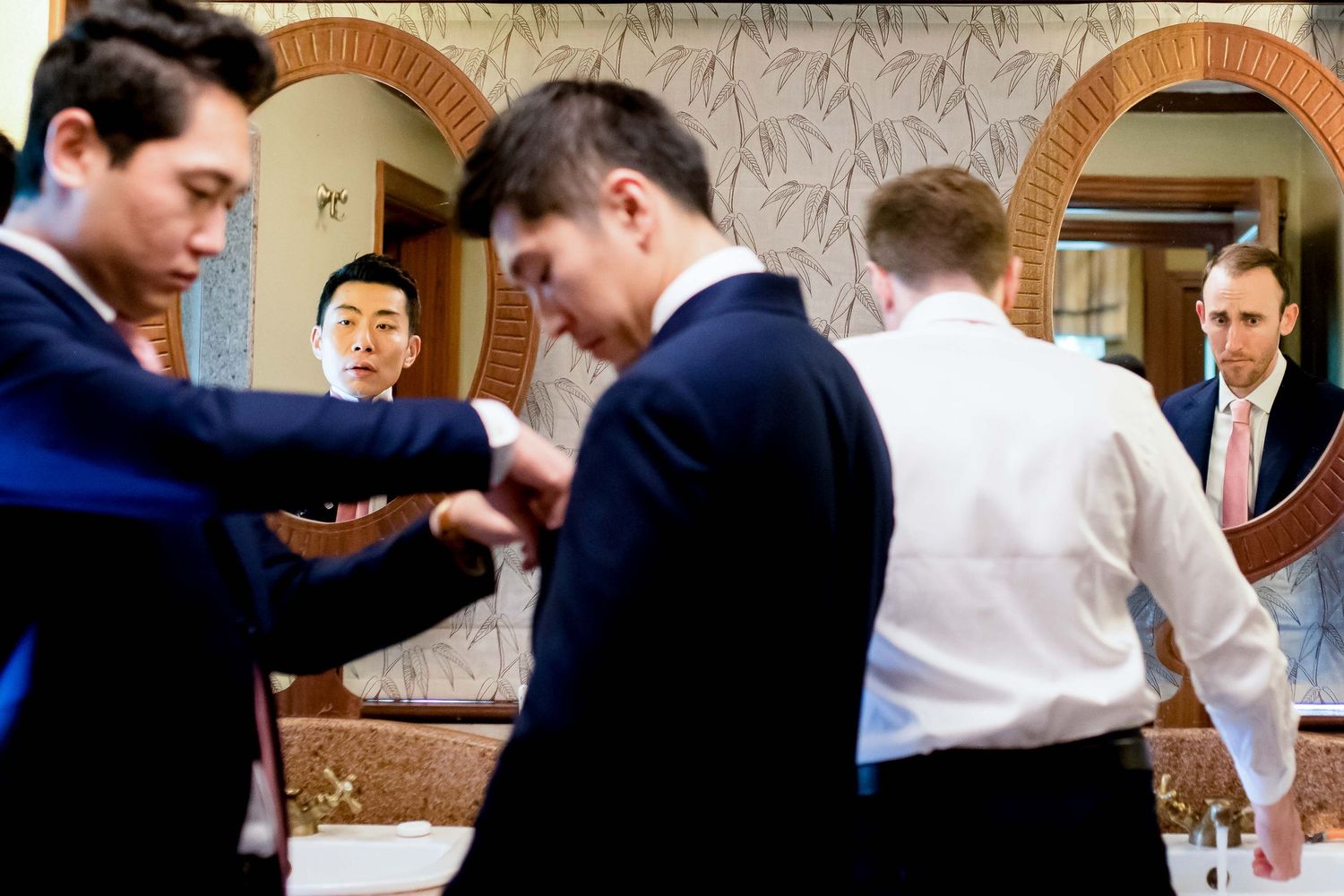 Group of formally dressed people helping each other prepare in a room with arched doorways.