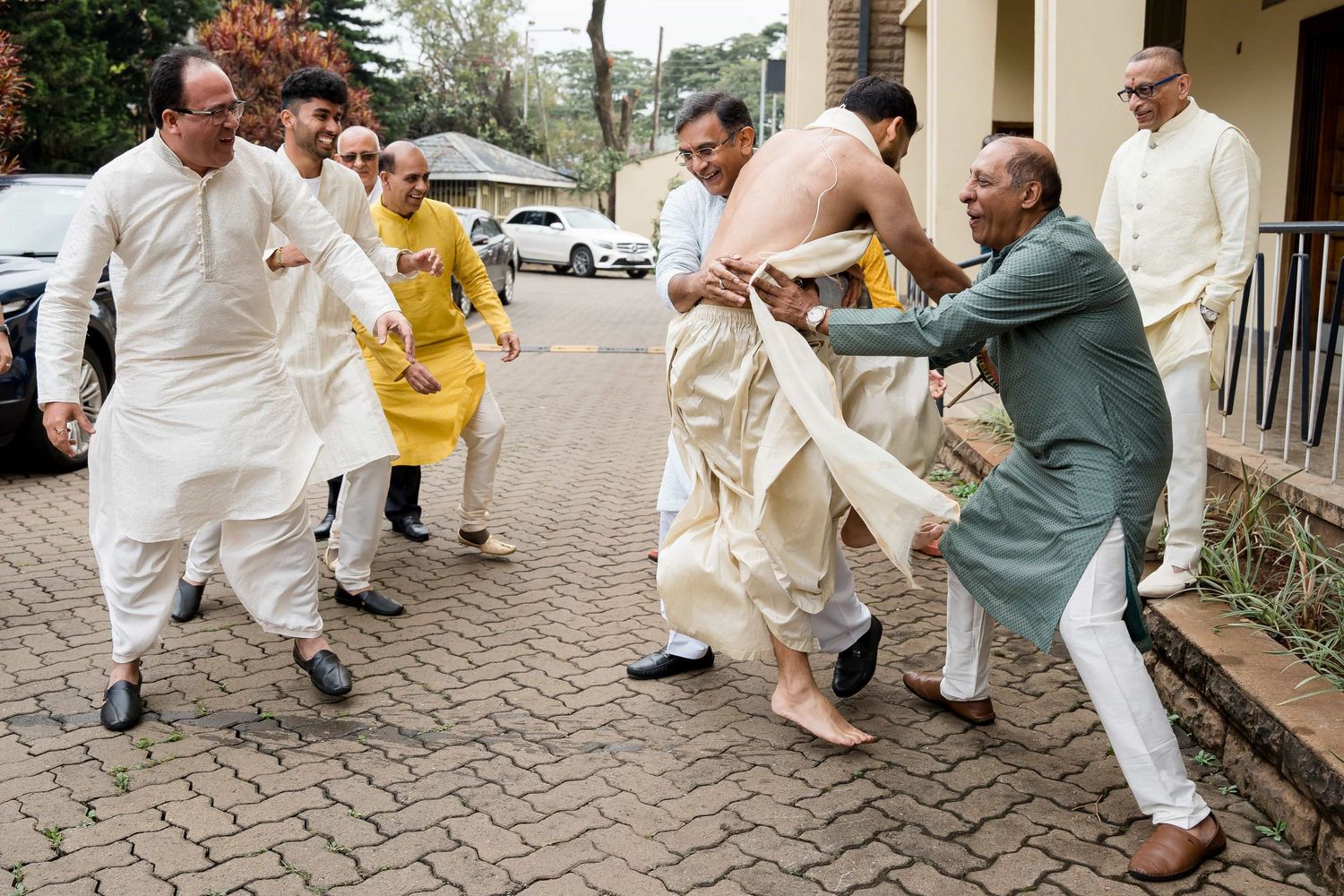 A lively group of people in white and colored outfits dance energetically on a brick pathway.