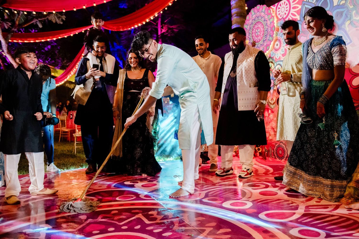 People dancing on a colorful illuminated dance floor at a festive celebration with red and pink lighting effects.