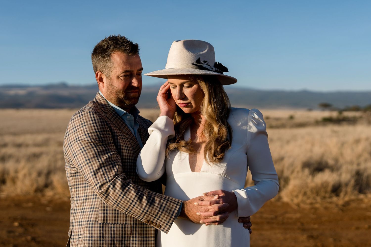Couple in western wedding attire sharing an intimate moment in a desert setting.